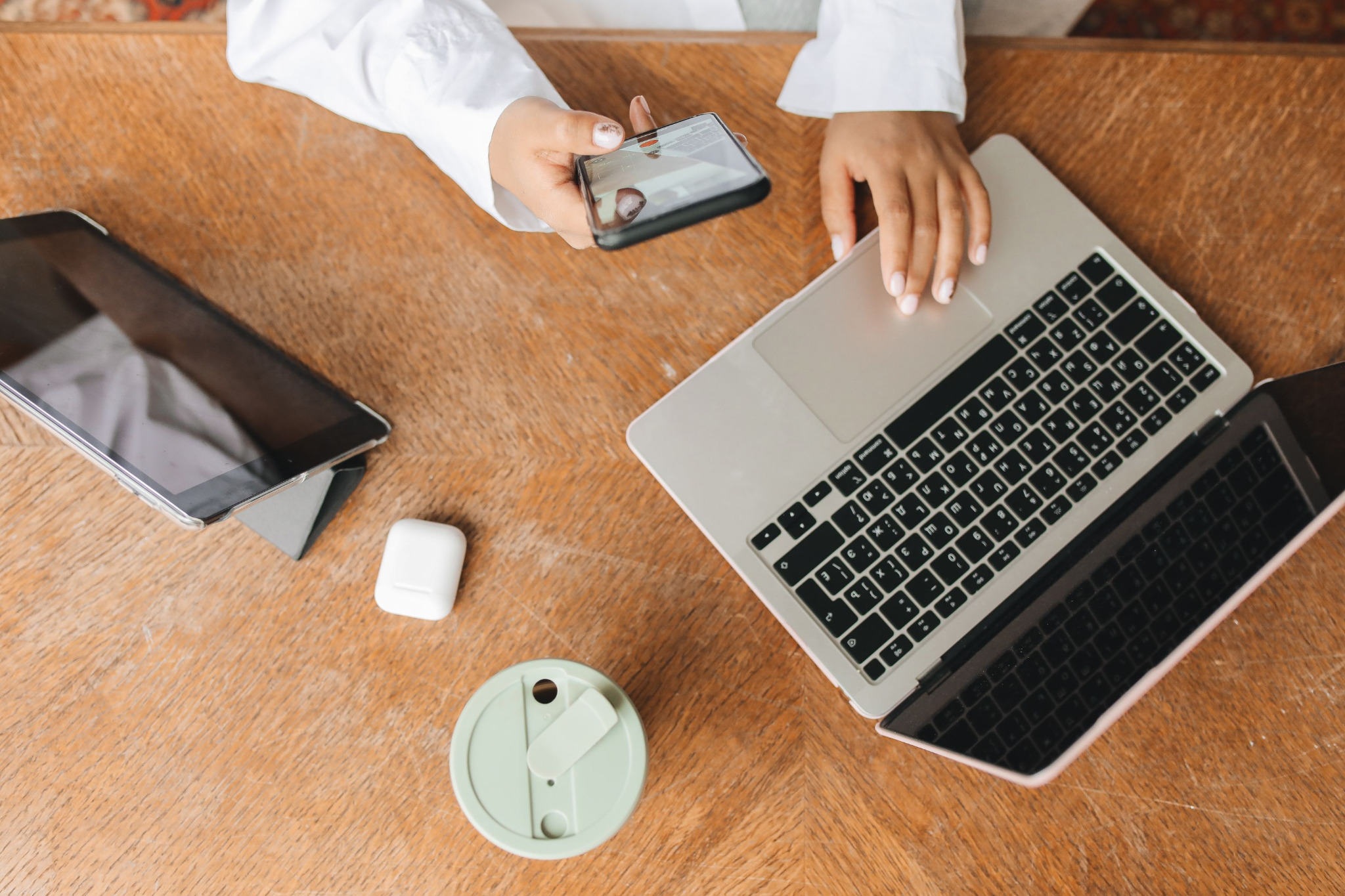 Hands using a laptop and phone at a wooden workspace